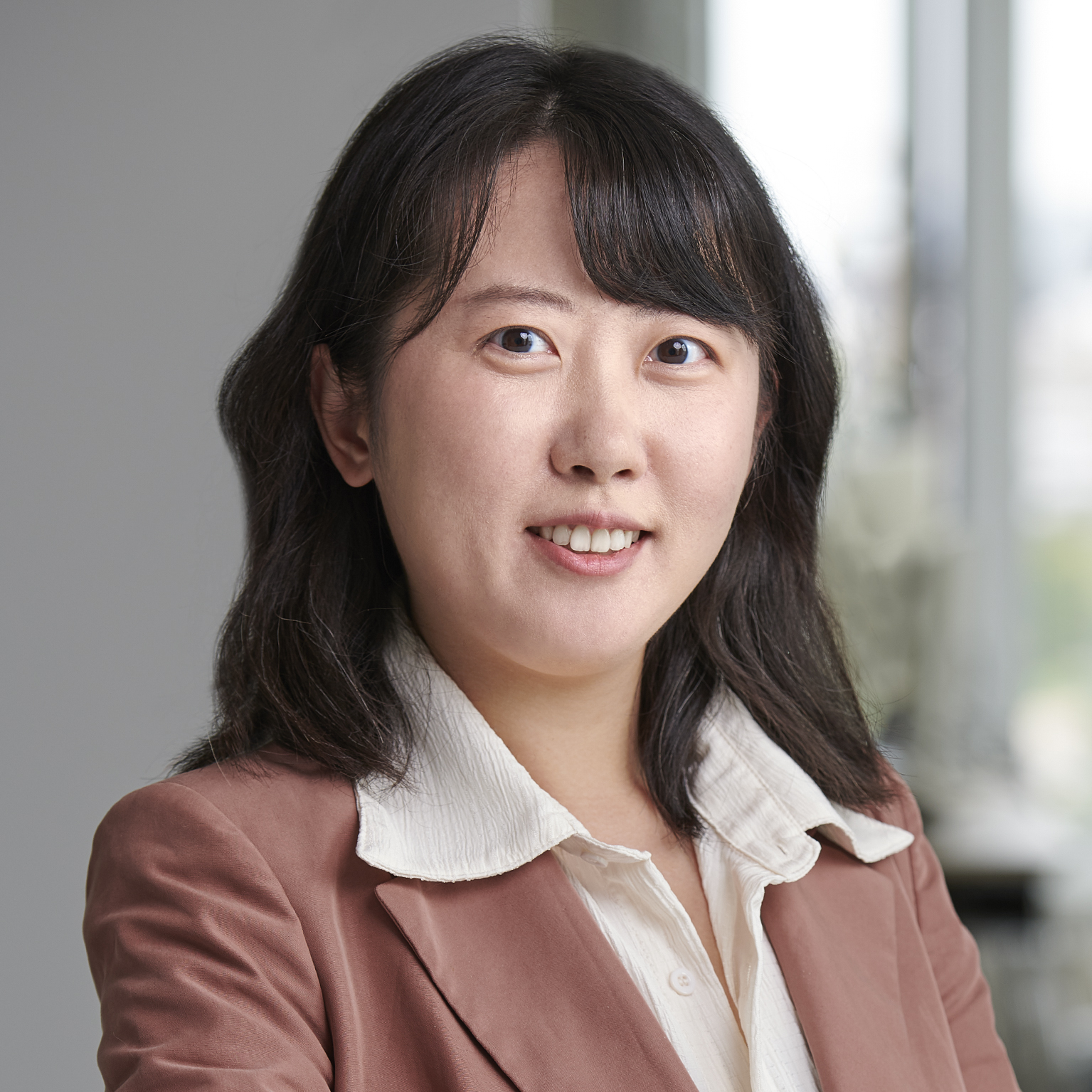 Junjiao Ma, Patent Professional for Electrical Engineering at EHF IP, wearing a white shirt and brown blazer in front of a bright window background.